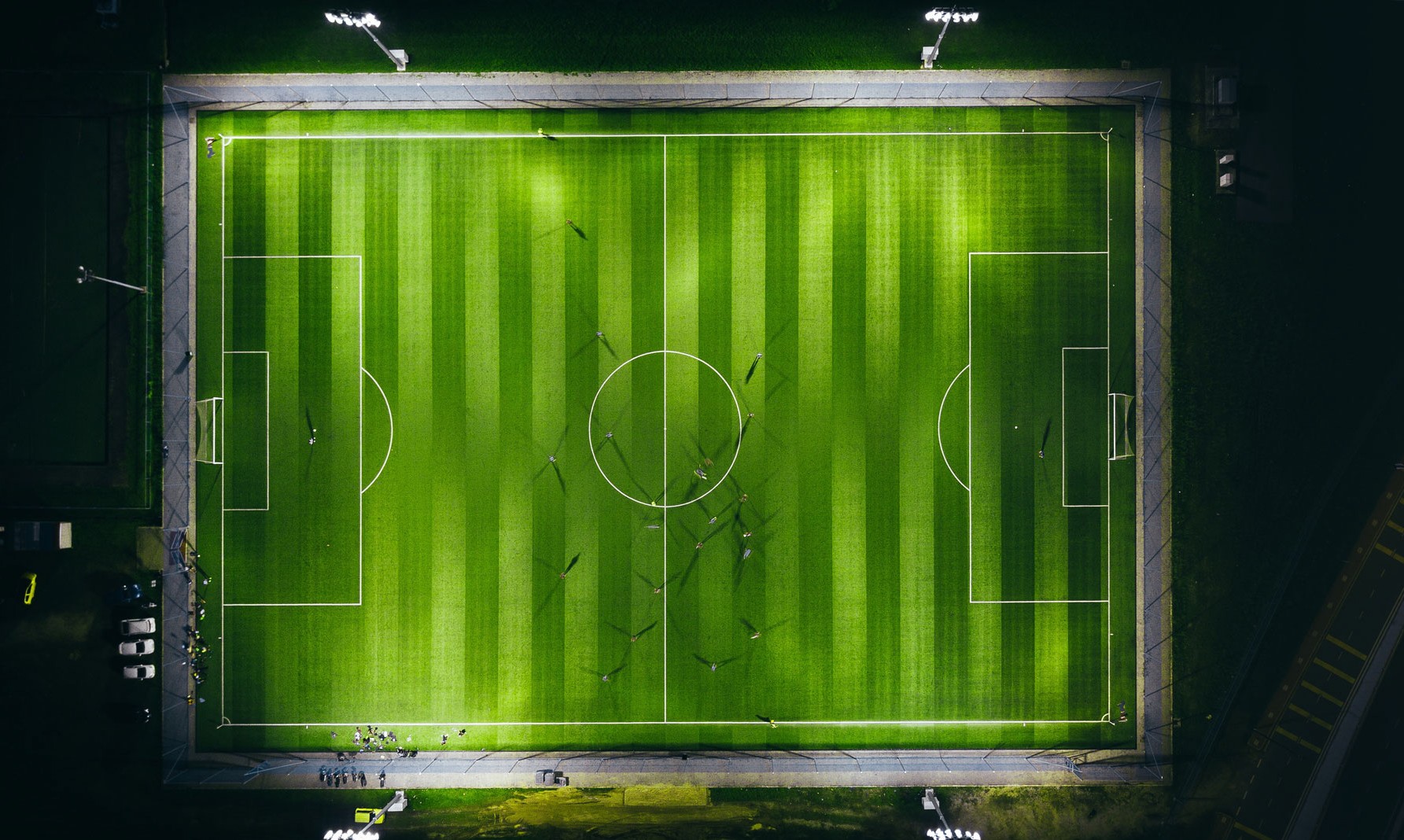 Floodlit community sports field at night, viewed from above during a match