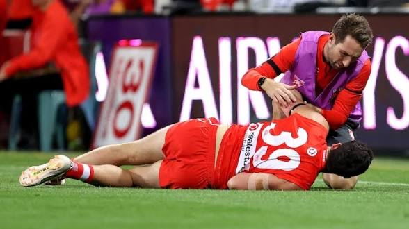 A medical staff member assessing a downed player on the field during a match